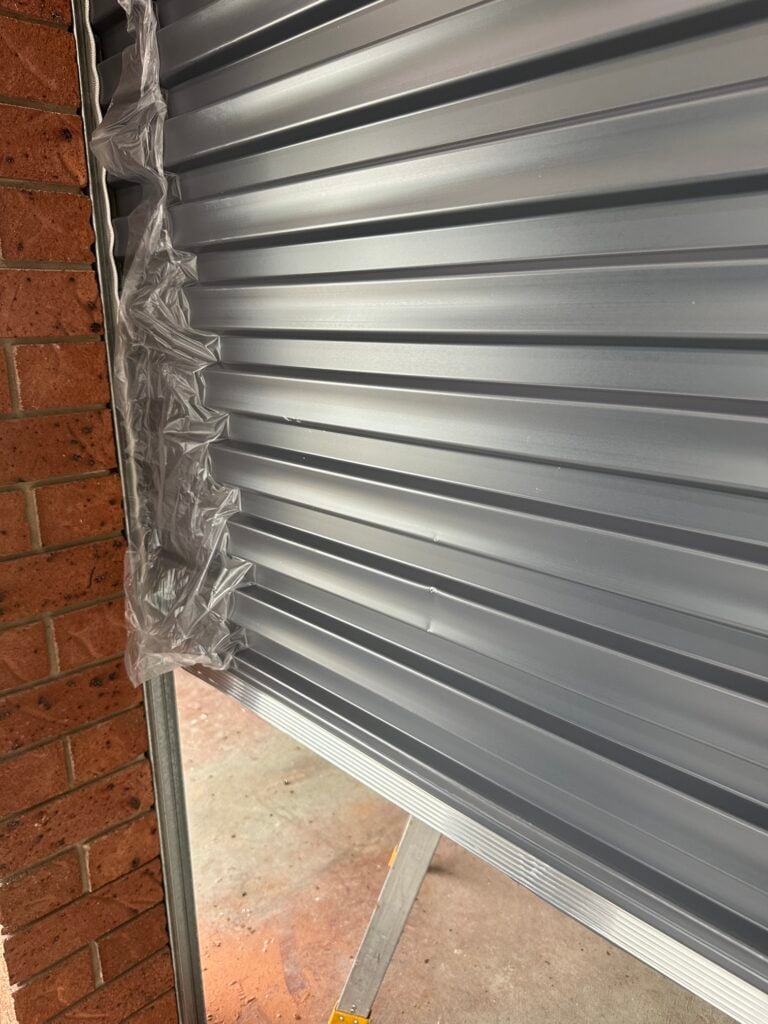 Close-up of a grey roller shutter and brick wall.