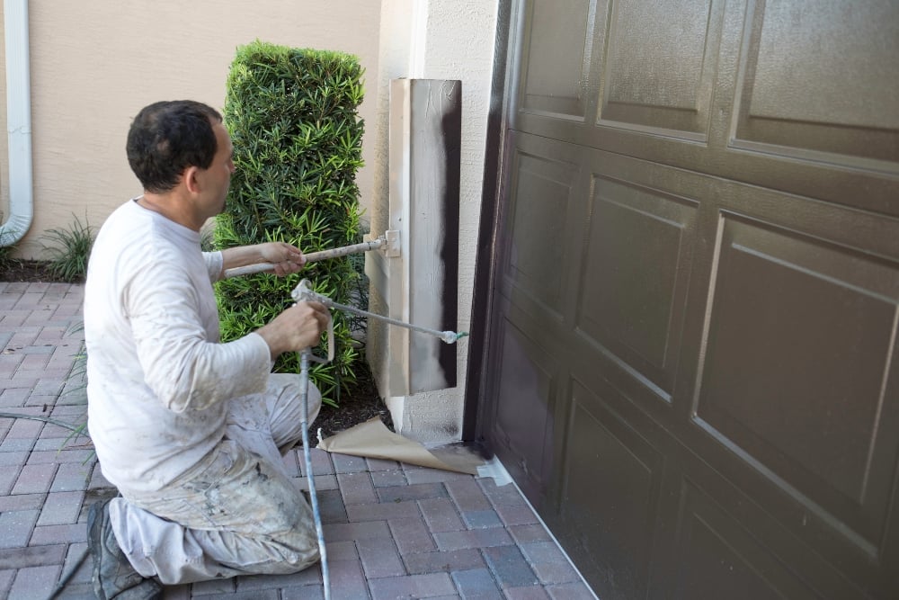 Man spray painting garage door frame exterior