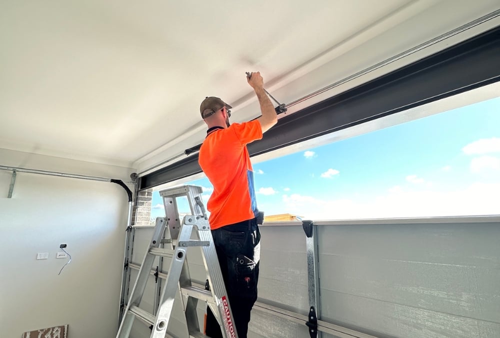 Technician repairing garage door on ladder indoors