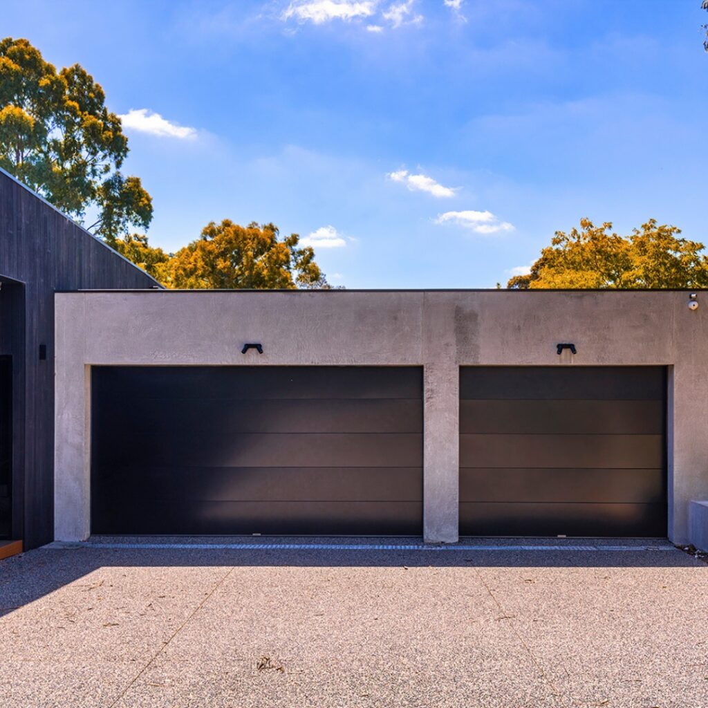 Modern home with two black sectional garage doors set into a smooth concrete exterior.