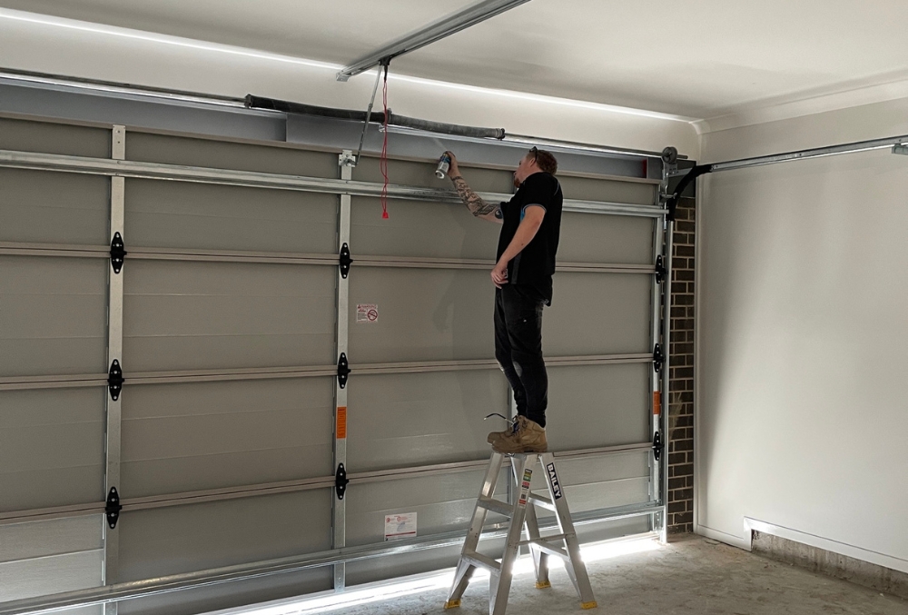 Man on ladder repairing garage door mechanism