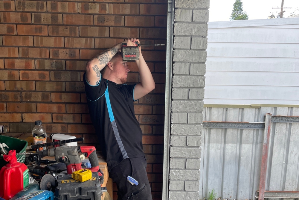 Tradesman drilling into brick wall outside house