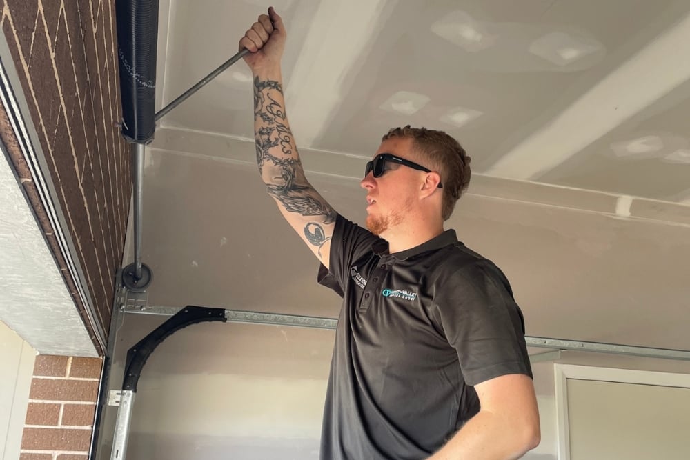 Technician adjusting garage door mechanism with rod