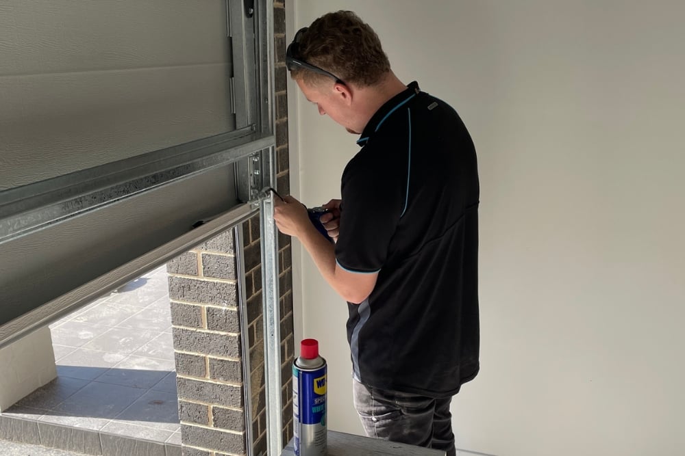 A technician performing maintenance on a sectional garage door track in a Newcastle home.