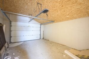 Empty garage with white garage door and debris
