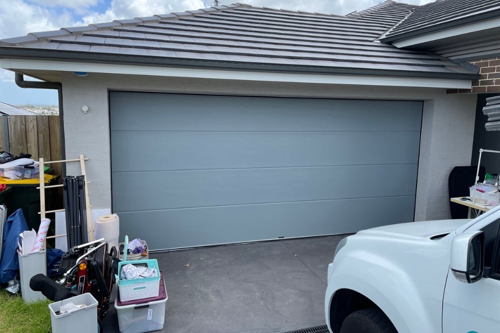 Closed grey garage door with cluttered driveway and ute