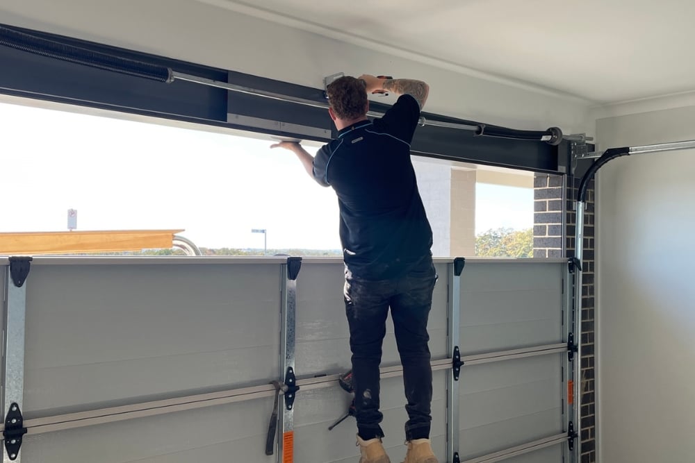 Worker standing on a garage door panel to perform overhead maintenance.