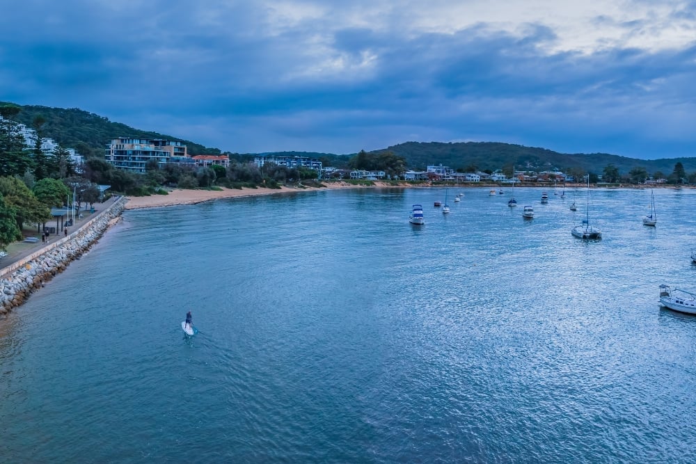 Coastal bay with boats and paddleboarder at dusk
