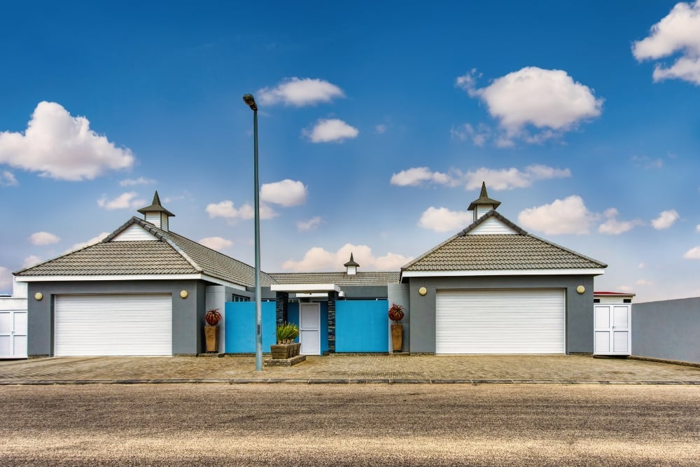 A modern duplex featuring two grey garage units with white roller doors