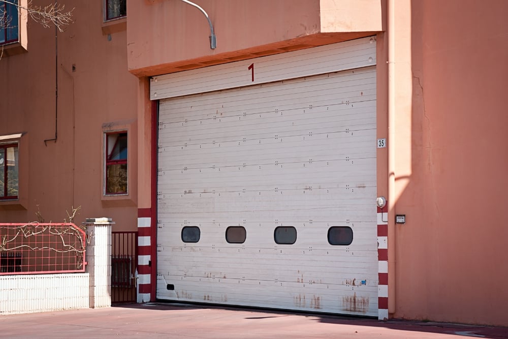 A large, weathered white sectional garage door with small rectangular windows and rust stains at the base