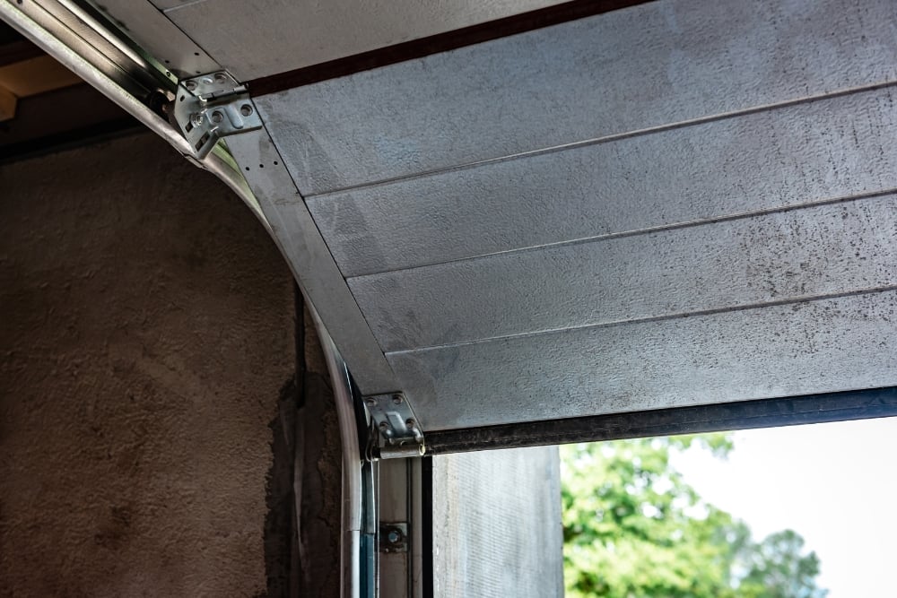 Close-up of the metal hinges, rollers, and tracks on an open sectional garage door.