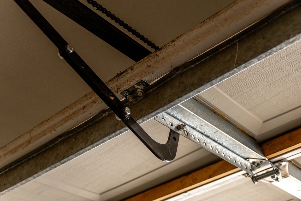 Close-up view of a worn garage door opener mechanism, showing the metal tracks, trolley arm, and chain drive system.