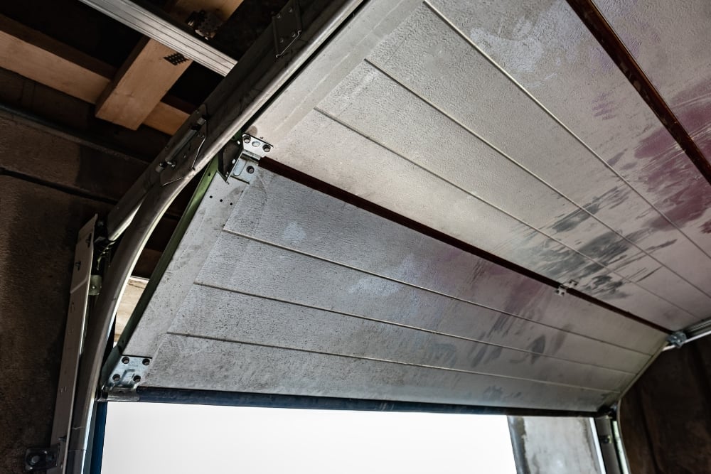 Low-angle shot looking up at the hinges, brackets, and underside panels of an open garage door.