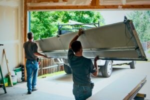 Two technicians manually lifting a large, single garage door panel into place during a replacement at a residential property.