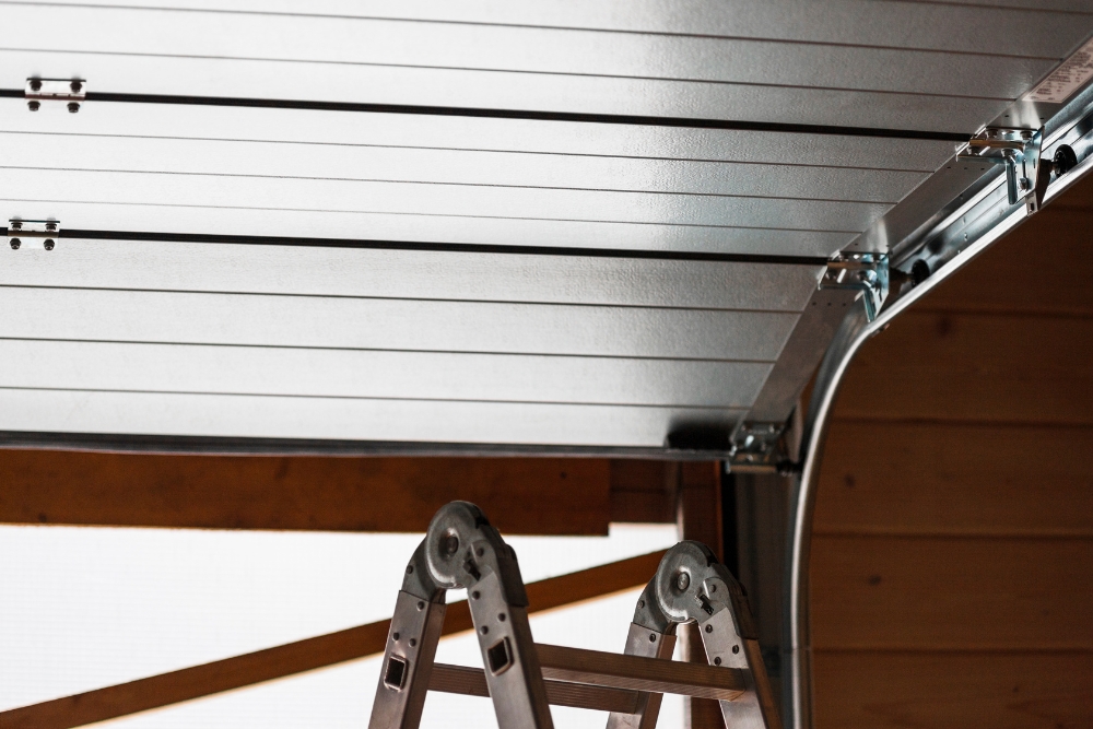 An interior view looking up at a partially open white sectional garage door resting on its overhead metal tracks.