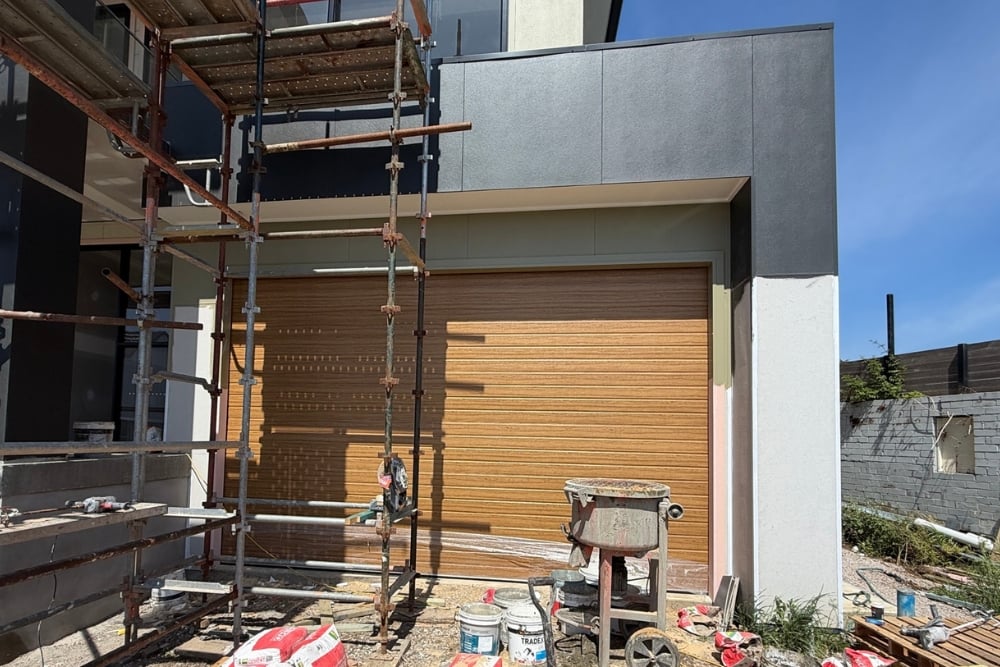 A wood-look sectional garage door installed on a modern house under construction