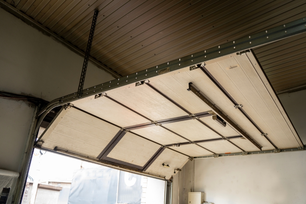 An open sectional garage door overhead, showing its tracks, hinges, and the interior framework of the panels.